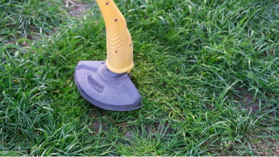 A yellow trimmer head cutting grass, showcasing an essential electric lawn mower accessory for precise edge trimming.